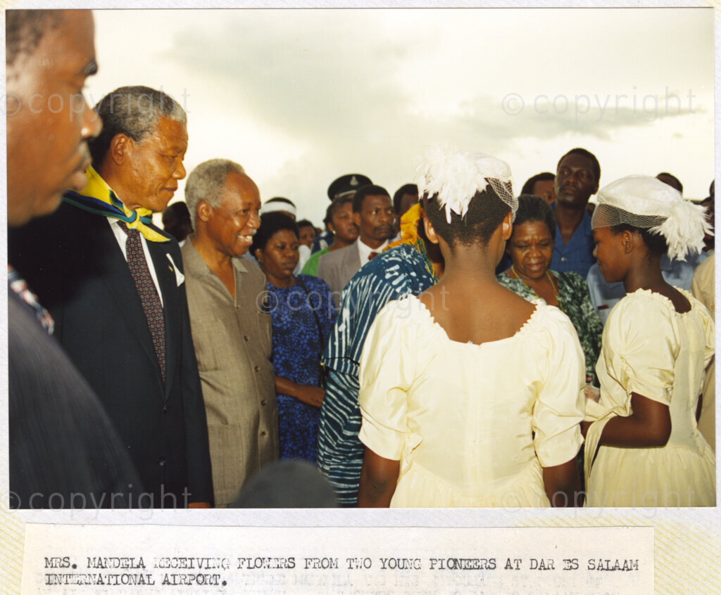 Dar Es Salaam, Tanzania. PHOTO: ANC Archives. 6 March 1990. Nelson Mandela (second left), deputy president of the African National Congress (ANC) and Julius Nyerere (third left), Chairman of the Chama Cha Mapinduzi (CCM), look on as Winnie Mandela receives a presentation of flowers from two Young Pioneers at Dar Es Salaam International Airport, in Tanzania. Mandela and his wife, Winnie, are on a tour of African states which support the liberation struggle in South Africa.