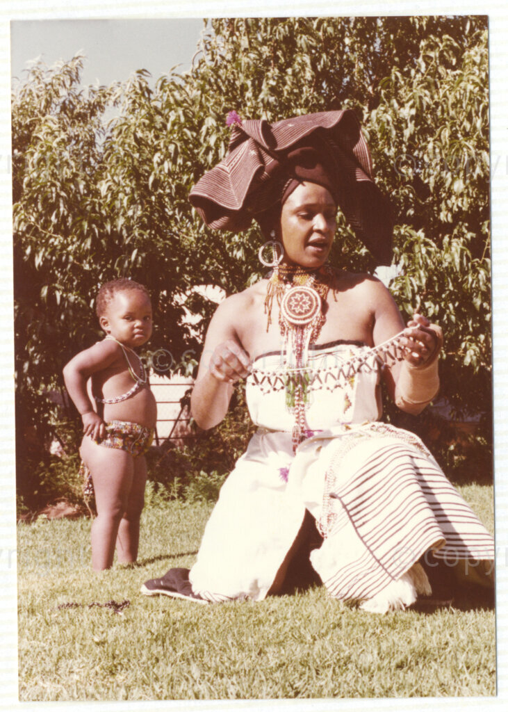 Winnie Mandela (right) and a young child (unknown), both wearing traditional Xhosa attire, circa 1980. Mandela was one of the most important icons of the struggle against apartheid in South Africa and wore traditional outfits and accessories during a time when donning cultural wear was seen as 
a political taboo. The outfits reflect the cultural heritage of her birthplace, Bizana, a rural town in the Transkei in the Eastern Cape.