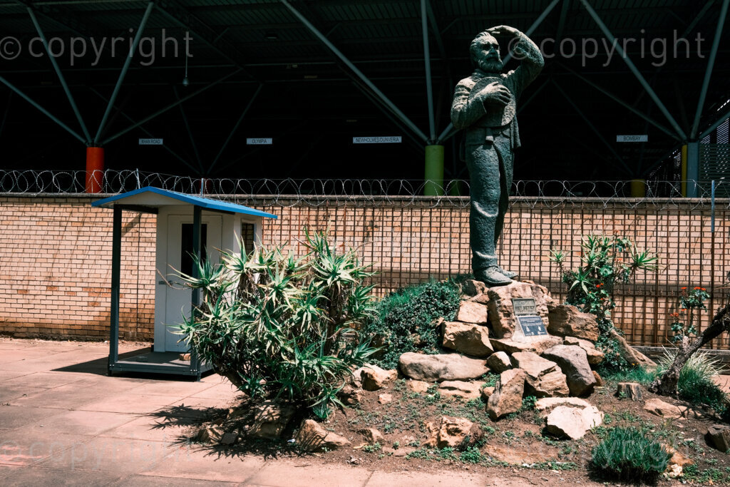 Figures in a 'Scape. Piet Retief was one of the leaders of the Great Trek. He proposed that Natal was one of the final destinations and selected a location for its future capital, later named Pietermaritzburg in his honour. The short-lived Boer republic Natalia was annexed and became a part of the British colony of Natal with Pietermaritzburg as the capital city. His sculpture stands in the grounds of the Msunduzi Museum with the Market Square Taxi Rank as a backdrop. Oct. 2024, Pietermaritzburg, South Africa.
