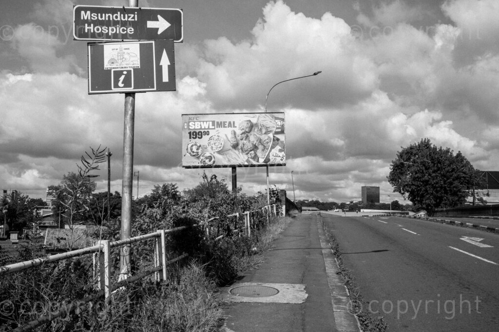 Some aspects of the city of Pietermaritzburg in KwaZulu-Natal, South Africa. Pietermaritzburg is one of the oldest cities of South Africa, the city fathers like to call it the City of Choice. The photographer John Robinson ended up back in the city when he had to leave Johannesburg while walking into the mist seeking out a dignified and beautiful place.

Pietermaritzburg is not a perfect city by any standards, it is located in a geographical bowl straddling the Msunduzi River, it is a juxtaposition of many people and things. A city that many people just pass on their way to and from the cities of Durban and Johannesburg on the bisecting N3 highway.

All these spaces are public or easily accessible to all the people of Pietermaritzburg. Though many people in this city prefer to live out their lives behind their own high walls or in office parks and malls that have visible security. Non the less these spaces remain as evidence of human intervention. 2023, Pietermaritzburg, KwaZulu-Natal, South Africa.