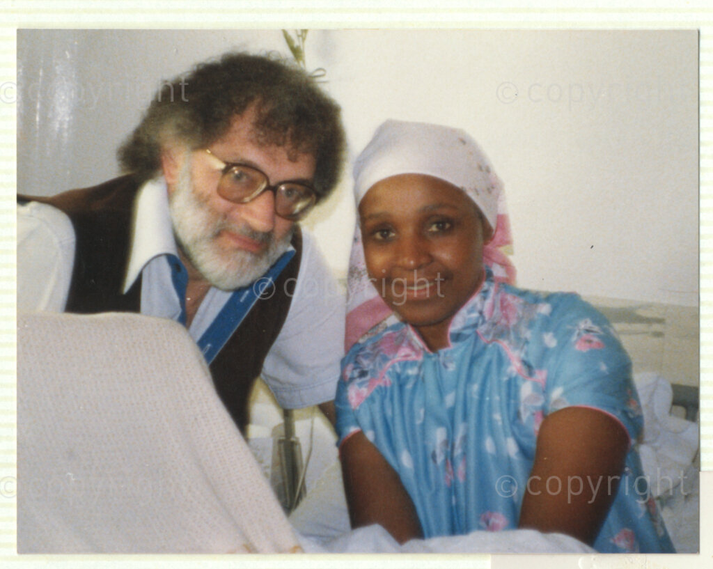 Winnie Mandela (right) and an unidentified man (left) look relaxed in what appears to be a hospital environment, circa 1980. Winnie is wearing a colourful nightgown and white head scarf, and the man wears thick-rimmed spectacles. Winnie was one of the most important icons of the struggle against apartheid in South Africa.