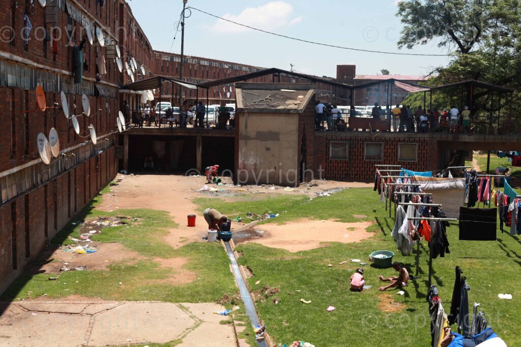 A woman doing washing at the Madala Hostel in Alexandra, Johannesburg in Gauteng, South Africa while the kids are playing around the washing line on 04 Dec 2022. Photo: Oupa Nkosi 