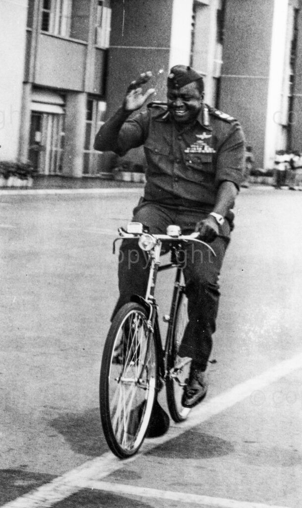 Field Marshal Idi Amin Rides Amok – conqueror of the British Empire, inspects his air force on a bicycle because there is no petrol for his motor car.