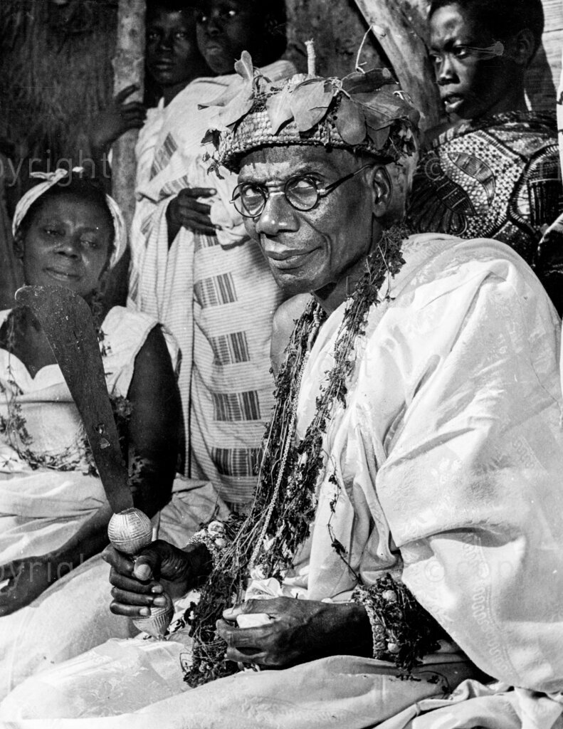 Great Day For Elmina – Paramount Chief with dagger. This year annual celebrations were blessed with presence of Paramount Chief Nana Condua IV, who was dressed in symbolic garb, clutching decorated dagger. This has always been a great annual ceremony for the Elminians ever since the legendary priestess Etsi Ekua returned from the dead to teach the tribe how to propitiate the river god, Benya. Whether you believe in it or not it provides the people with a holiday and much merrymaking. Once a year the Elminian men, women and children gather in their thousands on the banks of the River Benya in their best clothes to watch the chief priest propitiate the river god of the State, Benya.