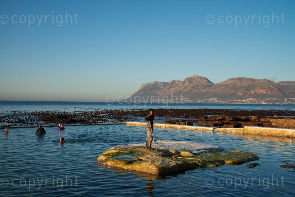 People swim as a worker removes slippery algae by painting lime wash on a rock in the Dalebrook tidal pool in Kalk Bay. While public spaces, in theory, are closed under Level 3 lockdown regulations, much of the public seemed to have decided that these spaces are now open. Workers could also be seen tidying up some of these spaces today, Wednesday June 24, 2020. The city of Cape Town has appealed to the national government to ease the lockdown on public spaces, and it appears they may be preparing for re-opening. PHOTO: EVA-LOTTA JANSSON