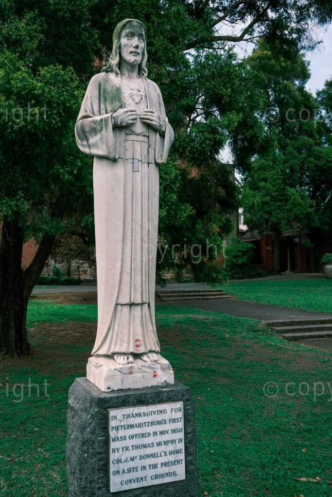 Figures in a 'Scape, the kissed feet of the thanksgiving figure of Christ in front gardens of the St Mary’s Catholic Church. Nov. 2024, Pietermaritzburg, South Africa.
