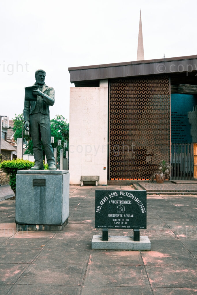 Figures in a 'Scape, a bronze statue of Gert Maritz outside the Ned. Geref. Kerk or as it is also known Voortrekker Kerk on Church Street in the CDB of the city of ‘Maritzburg. Nov.2024, Pietermaritzburg, South Africa.