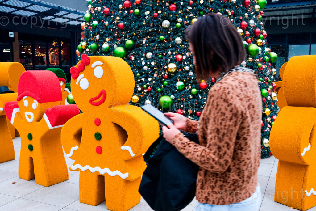 Christmas ginger bread men. Woman with mobile phone walking past Christmas display outside shopping center. 17 Dec. 2024, Pietermaritzburg, South Africa.