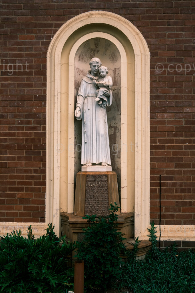 Figures in a 'Scape, the figure of St Antony of Padua and child in an alcove of the front wall of the Marian Center in Jabu Ndlovu Street. The Marian Center now houses a school for the children of the city. Nov. 2024, Pietermaritzburg, South Africa.